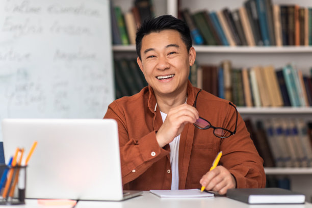 快乐的韩国男教师在笔记本电脑旁做笔记图片下载
