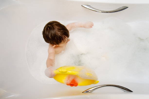一个快乐的孩子坐在自制的白色浴缸里玩玩具。蹒跚学步的小男孩在泡泡浴中洗澡。一岁六个月大的孩子图片下载