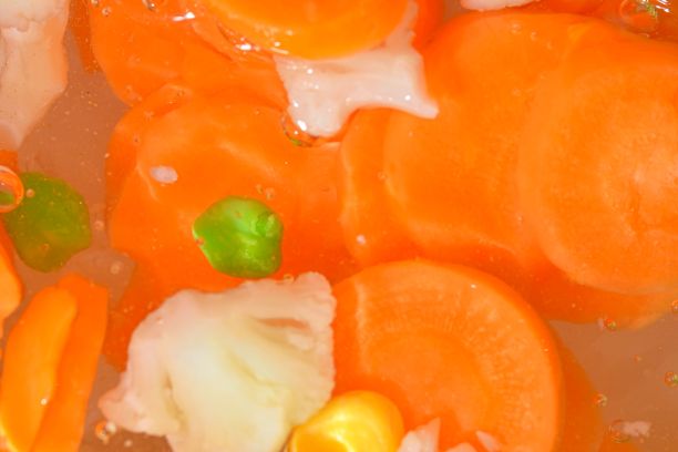 沸水加新鲜蔬菜，特写。近景的汤蔬菜与胡萝卜，豌豆，花椰菜和玉米在水的背景。水煮蔬菜的质感，玻璃墙上有大气泡。平面设计，俯视图。水平的形象。图片下载