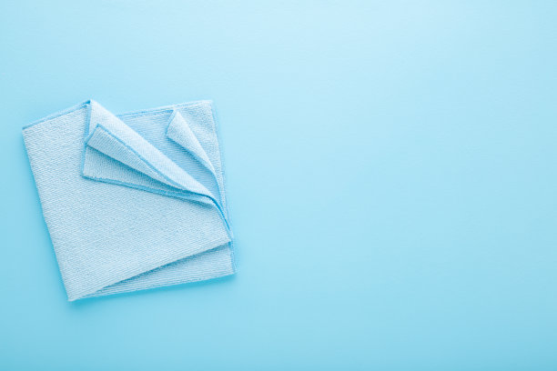 可折叠的干软超细纤维抹布，适用于不同表面，在浅蓝色的桌面背景上擦拭。柔和的颜色。特写镜头。文本的空白位置。自顶向下视图。图片下载