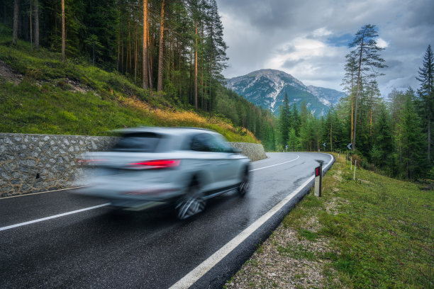 迷离的汽车在雨中绿色森林的道路上行驶。白云石山脉,意大利。在阴雨天完美的山路。意大利阿尔卑斯山上的松树。交通工具。木材公路图片下载