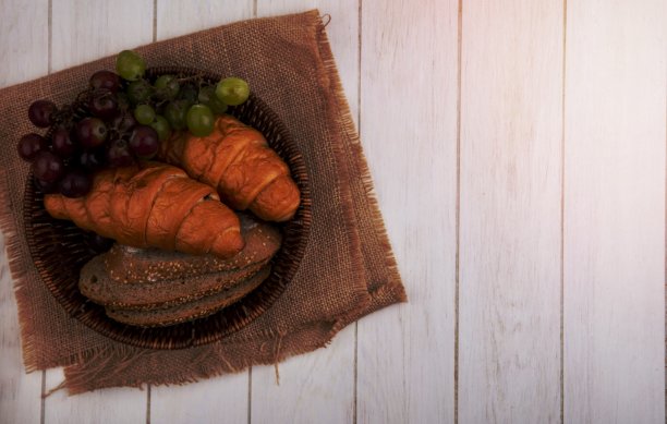 面包的顶视图牛角面包和种子的棕色玉米棒面包片与葡萄在篮子上的布袋上的木制背景与复制空间图片下载