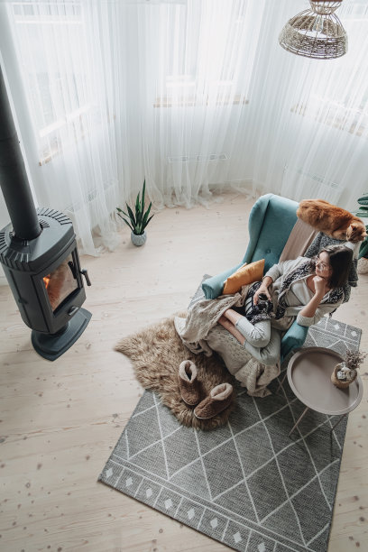 年轻的女人坐在舒适的扶手椅和格纹坐在壁炉旁和一只家猫，在家里喝茶图片下载