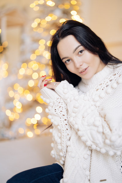 年轻女子的肖像对圣诞发光花环的背景。图片下载