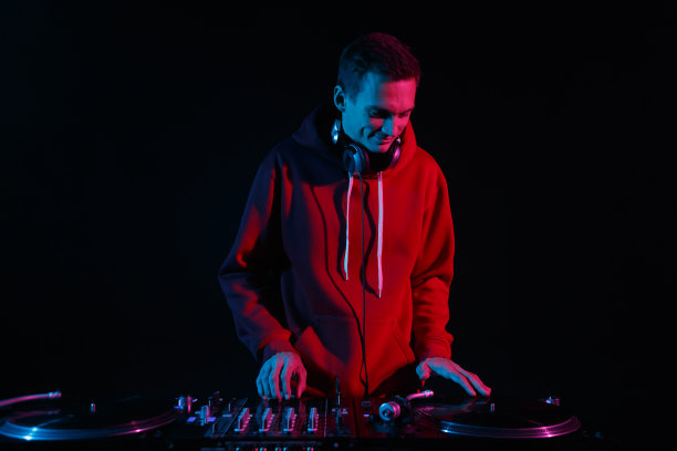 欢快的年轻DJ刮黑胶唱片派对在夜总会。酷酷的白色唱片播音员在舞台上微笑着播放音乐图片下载