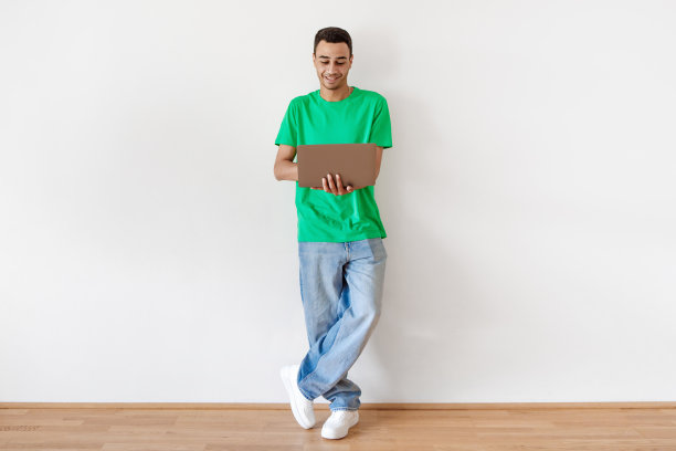 在线教育项目。快乐的阿拉伯自由职业者男子与笔记本电脑在手中站在光墙，全长拍摄图片下载