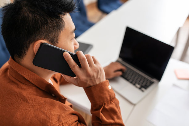 亚洲商人在办公室用笔记本电脑打电话图片下载