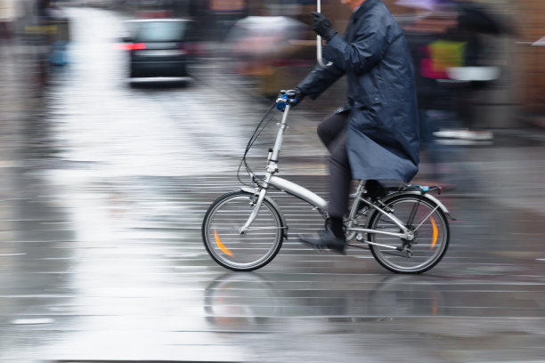 男子带伞骑折叠自行车在下雨的城市图片下载