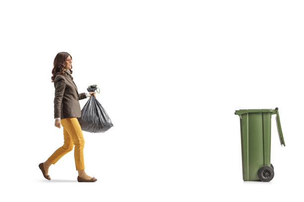 一名穿着正装的年轻女子拿着一个塑料垃圾袋，走向垃圾箱图片下载
