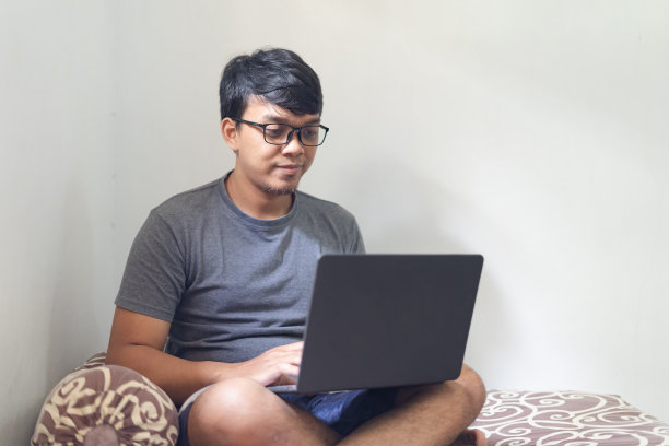 肖像严肃的亚洲眼镜男子看着笔记本电脑在卧室工作的概念与自然光线图片下载