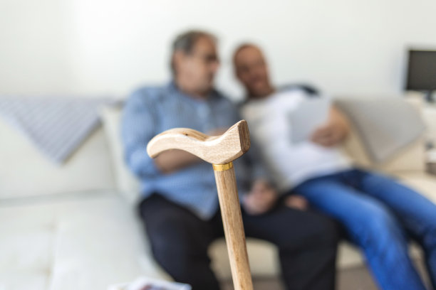 一个成年的时髦儿子和年长的父亲坐在家里的楼梯上，看着照片。年长的父亲和成年的儿子在家里聊天和看照片。图片下载