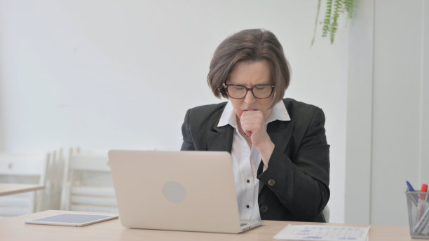 老女商人在笔记本电脑上工作时咳嗽图片下载