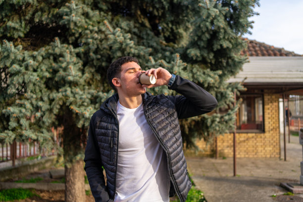 年轻男子站在外面喝外卖咖啡-资料照片。图片下载