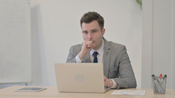 年轻的商人在笔记本电脑上工作时咳嗽图片下载