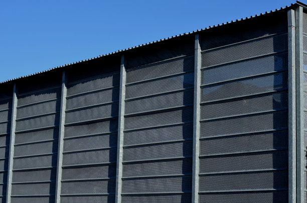 带有扩展金属晶格结构的建筑物的钢包层。镀锌灰色网保护工业建筑。蓝色的天空与银色的仓库背景形成对比图片下载