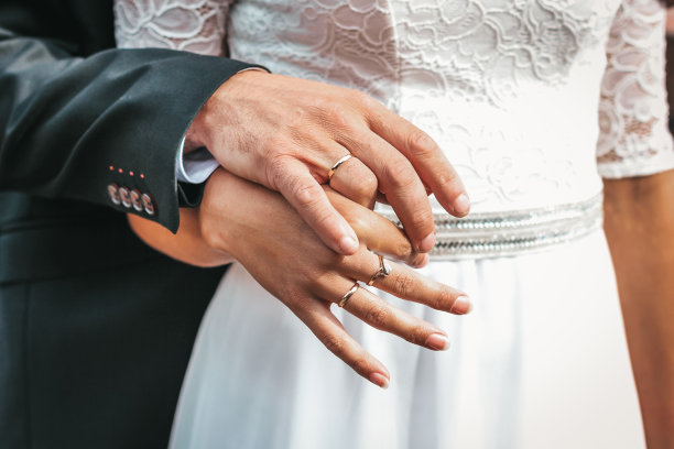 新娘和新郎的手的特写照片，上面装饰着结婚戒指。他们交缠的手指的美丽。新娘和新郎手上的戒指图片下载