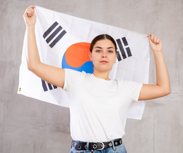 自信的年轻女子拿着韩国国旗对着灰色的墙图片下载