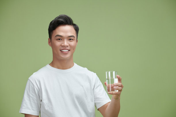 一个穿着白t恤的年轻帅哥手里拿着一杯饮用水图片下载