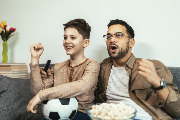 男孩和爸爸坐在家里的沙发上看足球比赛图片下载