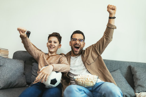 男孩和爸爸坐在家里的沙发上看足球比赛图片下载