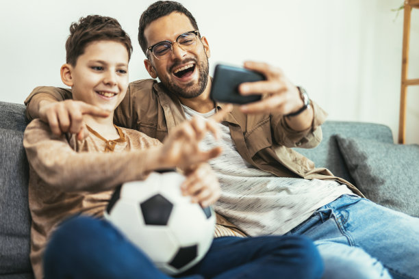 男孩和爸爸坐在家里的沙发上看足球比赛图片下载