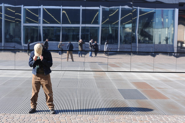一个戴着帽子的男孩作为一个模特站在有窗户的玻璃墙前，他的头低着，在一个场景拍摄行为图片下载