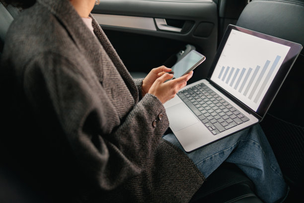 在去办公室的路上，女分析师坐在汽车后座上用笔记本电脑和手机工作的特写镜头图片下载