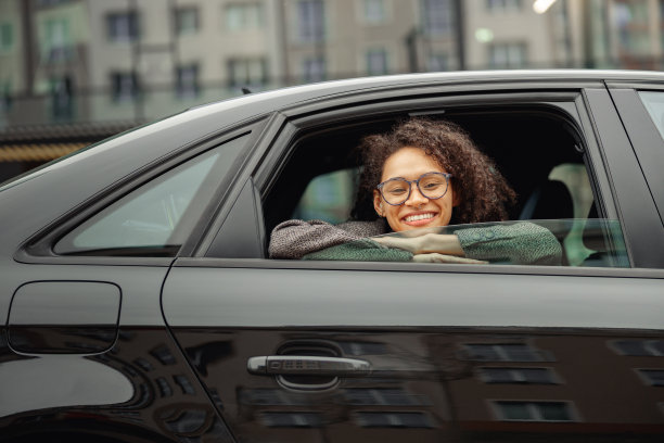 微笑的年轻女子戴着眼镜坐在城市出租车，看着窗户的肖像图片下载