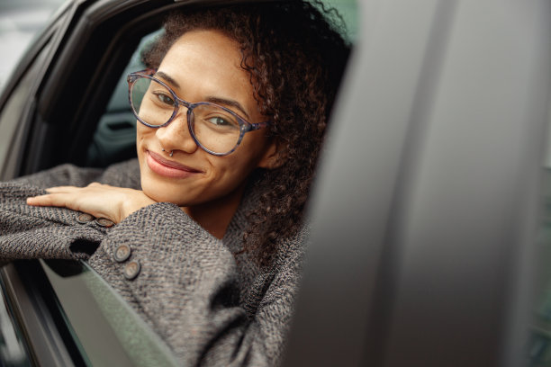 微笑的年轻女子戴着眼镜坐在城市出租车，看着相机的肖像图片下载