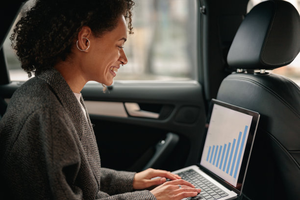 快乐的女经理在笔记本电脑上工作，坐在汽车皮革后座去办公室的路上图片下载