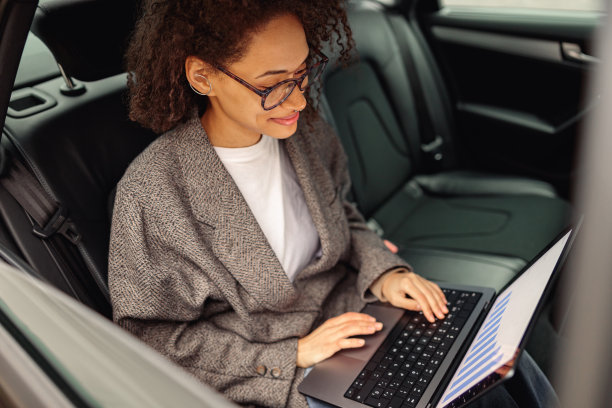 微笑的女商人经理在笔记本电脑上工作，坐在汽车皮革后座去办公室的路上图片下载