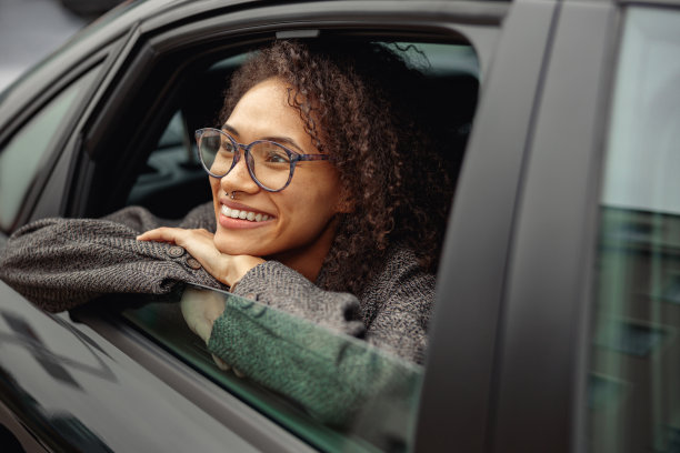 微笑的年轻女性办公室职员戴眼镜坐在城市出租车，看着窗户图片下载