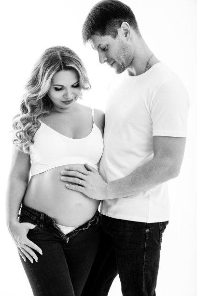 一对穿着白色背景的白色t恤和牛仔裤的夫妇在等待一个孩子。图片下载