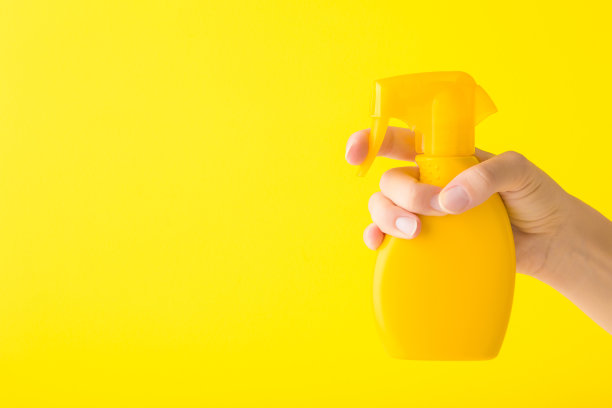 年轻的成年妇女手拿喷雾瓶防晒或清洁洗涤剂在明亮的黄色墙壁背景。特写镜头。文本的空白位置。侧视图。图片下载
