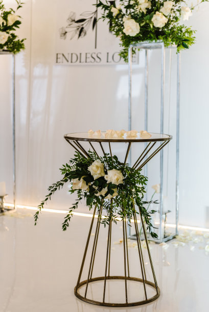 用鲜花和绿色植物装饰。豪华别致的婚礼桌。婚礼仪式，桌上放着钱箱和戒指。以拱门或照片墙为背景的架子。图片下载