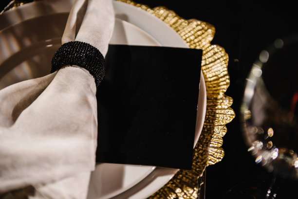 邀请函，客人座位，文字空间。白色的盘子，金色装饰的亚麻餐巾，黑色桌布上的酒杯。安装细节。餐桌布置，服务于大堂餐厅。前视图。特写镜头图片下载
