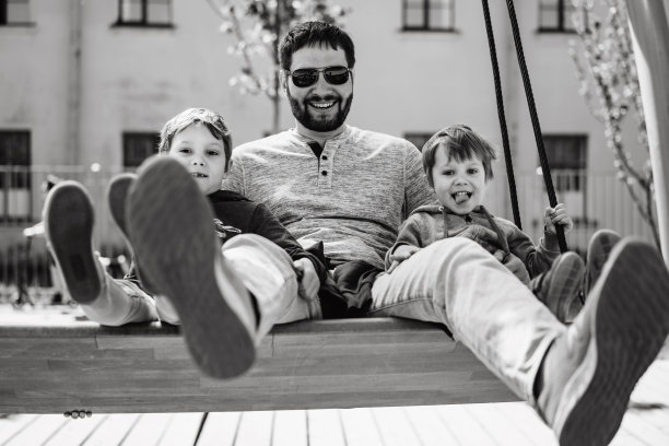 父亲和两个儿子一起在长椅上荡秋千。爸爸正在动他的腿图片下载
