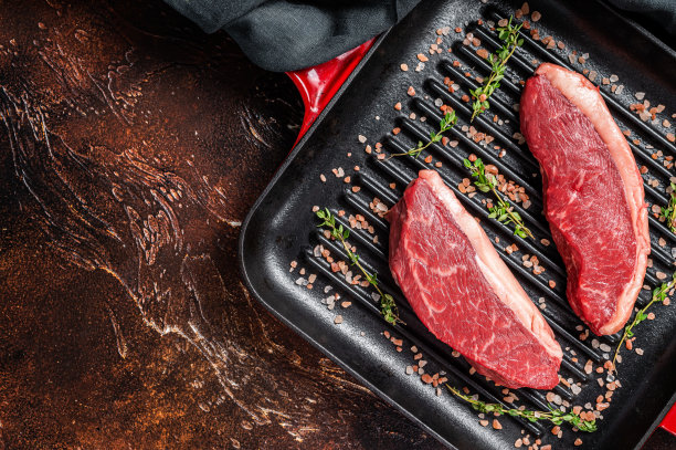 西冷牛排或巴西Picanha，生的大理石牛肉放在烤锅上。黑暗的背景。前视图。本空间图片下载