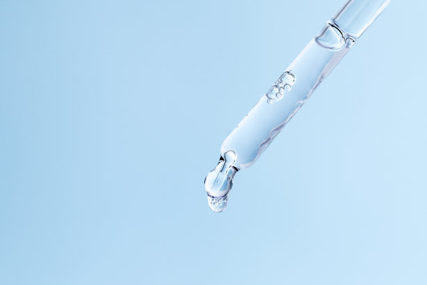 玻璃移液管与面部精华滴在蓝色背景。带有气泡的液体护肤化妆品特写。精油滴宏。透明质酸皮肤治疗滴管图片下载