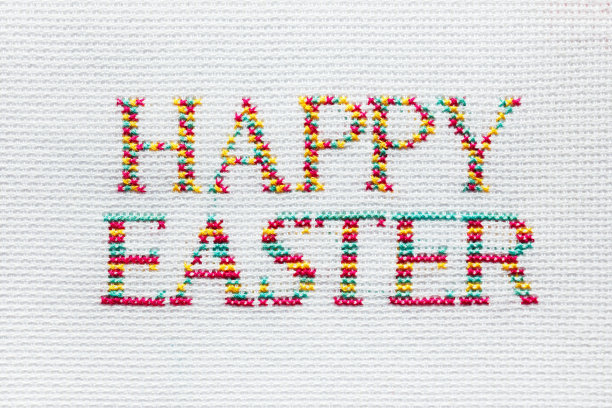 “复活节快乐”的铭文是用彩色线绣在白色织物上的。图片下载
