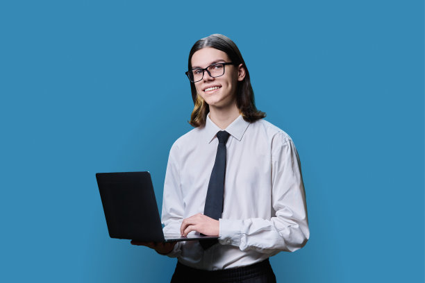 十几岁的大学生摆姿势与笔记本电脑在蓝色背景图片下载