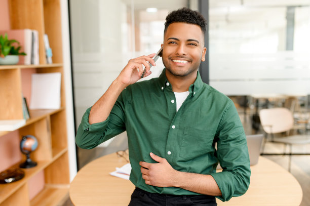 帅气的印度商人穿着休闲的绿色衬衫，在现代办公空间里用智能手机聊天图片下载