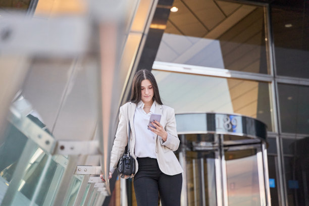 一名女子在办公楼外使用智能手机图片下载