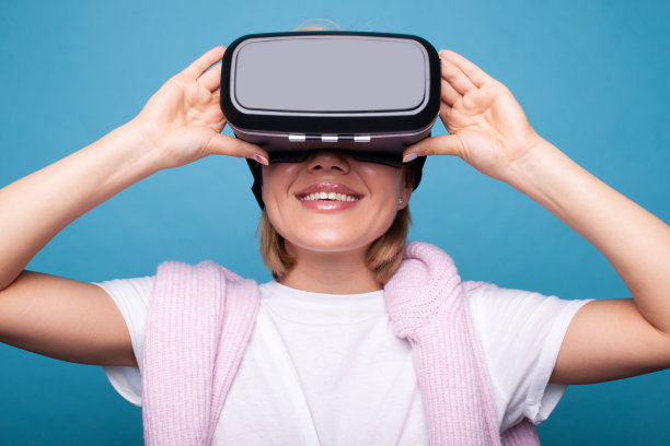 年轻的白人女子使用VR头盔，触摸眼镜，并在蓝色背景的虚拟现实中抬头。数码科技娱乐。现代技术。图片下载