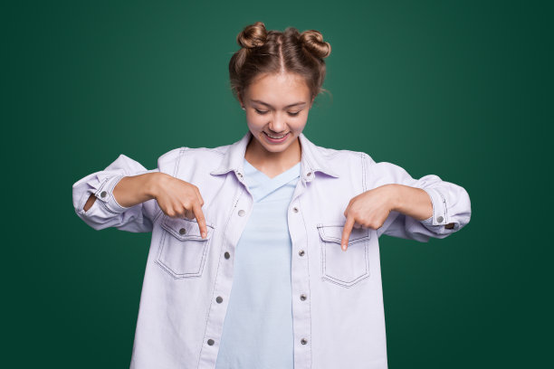 年轻女子指着手指向下和微笑的肖像，显示横幅，点击下面的链接手势孤立在绿色背景。图片下载