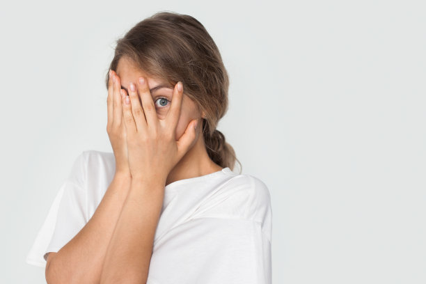 惊恐的白人妇女用手掌遮住脸，通过手指窥视一些孤立的白色背景与复制空间。图片下载