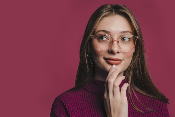 照片的年轻有吸引力的女人戴眼镜自信地看着远离孤立的深红颜色的背景。图片下载