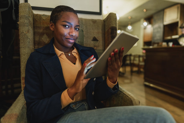 年轻的非洲妇女坐在扶手椅和使用数字平板电脑图片下载