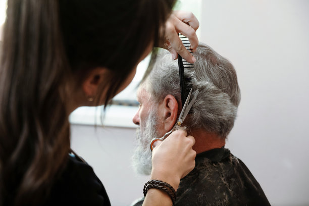 用剪子工作的手特写。专业的发型师女人剪成熟男人的头发。他正在理发店或美容院理发。图片下载