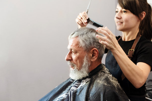 用剪刀工作。专业的发型师女人剪成熟男人的头发。他正在理发店或美容院理发。图片下载